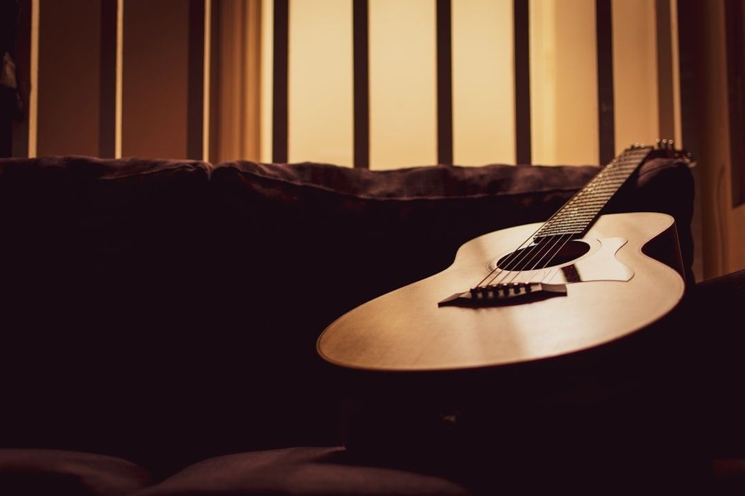 Akustisk gitar ligger på en mørk sofa i varmt kveldslys